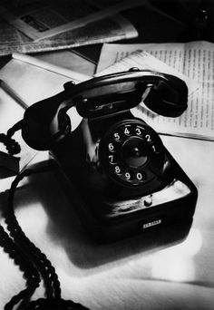 an old fashioned telephone sitting on top of a table next to some books and papers