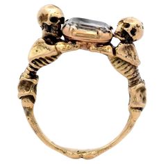 This Georgian style ring features two skeletons looking above and below while embracing a stuart crystal and is made from 18 karat gold. This statement ring features a colorless rock crystal, elevated by two intricately detailed skeletons. The skeletal figures embrace the stone together, creating an enchanting focal point. The band, also in yellow gold, echoes the skeletal design with refined features. A remarkable fusion of elegant, gloomy, and whimsical design. A bold choice for those who appreciate exceptional creativity in their jewelry. Signage: None but Size: 6.75 Condition: Excellent , with minimal signs of wear Year: Circa 1960 Weight: 10.0 grams total Please feel free to reach out with any questions, comments, or concerns. We will get back to you as soon as possible.  100% Money B Two Skeletons, Skeleton Jewelry, Gold Skeleton, Double Band Rings, Vintage Tiffany, Whimsical Design, Crystal Skull, Skull Ring, Rock Crystal