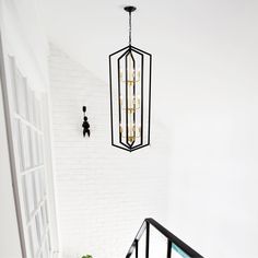 a light fixture hanging from the ceiling above a stair case in a white walled room