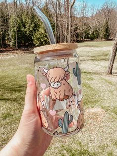 a hand holding up a mason jar with a straw lid and an animal on it