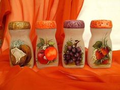 four salt and pepper shakers painted with fruit on them, sitting on an orange cloth