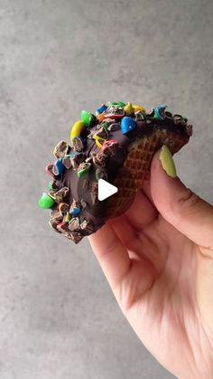 a person holding up a chocolate covered waffle with sprinkles on it