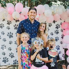 a man and two children standing in front of a backdrop with pink and white balloons