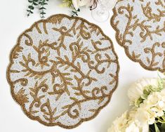 two white and gold doily with flowers on the table next to eachother