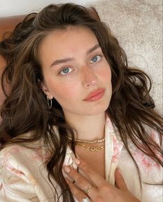 a woman with long brown hair wearing a white shirt and gold jewelry on her neck