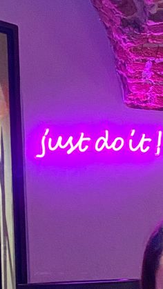 a woman standing in front of a neon sign that says just do it on the wall