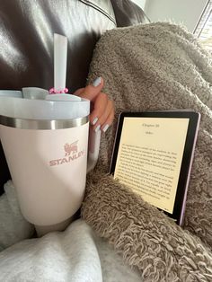 a woman sitting on a couch next to a book and cup with writing in it