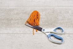 a pair of scissors sitting on top of a wooden floor next to orange string yarn