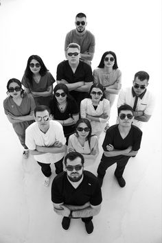 a group of people sitting next to each other in front of a white wall with sunglasses on