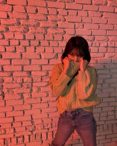 a woman standing in front of a brick wall holding her hands to her face and covering her eyes