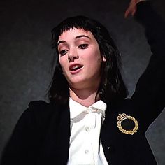 a woman in a black jacket and white shirt is holding her hand up to the side