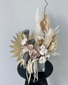 an arrangement of flowers and leaves on a table with a white wall in the background