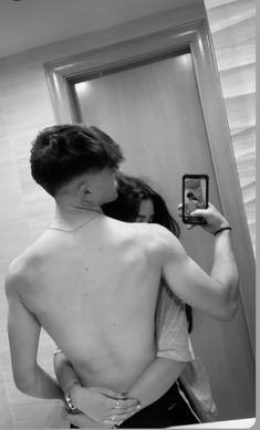 a shirtless man taking a selfie in front of a mirror with his back turned to the camera