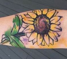 a sunflower tattoo on the arm with watercolors and green leaves around it