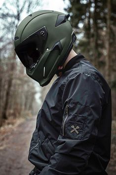 a man wearing a green helmet standing on a dirt road with trees in the background