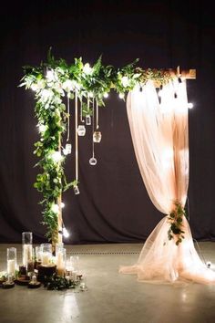 a wedding arch decorated with greenery and hanging ornaments is lit up by candles on the floor