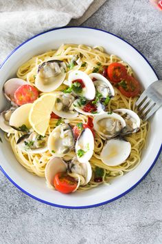 a white bowl filled with pasta and clams on top of a gray tablecloth