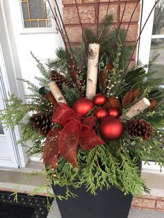 a planter filled with christmas decorations and greenery on the front door porch,