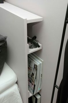 a white shelf with magazines on it next to a bed