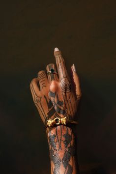 a hand with tattoos on it holding a gold ring