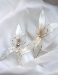 two white flower shaped earrings sitting on top of a white cloth covered bed sheet,