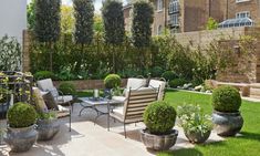 an outdoor patio area with chairs, tables and potted plants on the lawn in front of a brick building