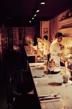 two chefs preparing food in a kitchen with candles on the counter and lights on the wall