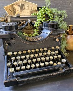 an old fashioned typewriter sitting on top of a table next to plants and pictures