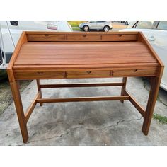 a wooden desk sitting on top of a cement floor next to a white car in a parking lot