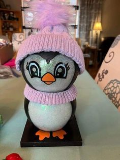 a small penguin wearing a pink hat and scarf on top of a wooden stand next to candy