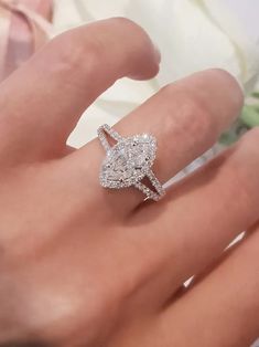 a woman's hand with a diamond ring on top of her finger, next to a bouquet of flowers