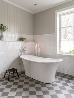 a white bath tub sitting next to a window in a room with checkered flooring