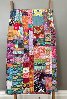 a multicolored patchwork quilt hanging up on a wooden easel in front of a gray wall