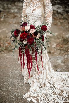 a woman in a white dress holding a bouquet of red and pink flowers on her wedding day