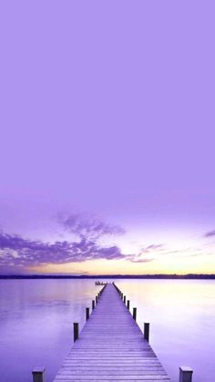 a dock that is sitting in the middle of some water at sunset with purple clouds