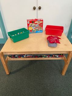 a wooden table with plastic containers and toys on it in front of a white wall