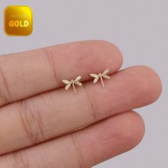 small gold dragonfly stud earrings on someone's finger