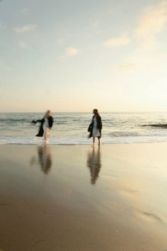 two people walking on the beach near the ocean