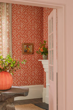 an orange vase filled with flowers sitting on top of a stone bench next to a doorway