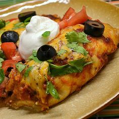 an enchilada with sour cream and black olives on a yellow plate