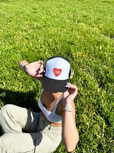 a woman sitting in the grass wearing a hat with a heart on it's side