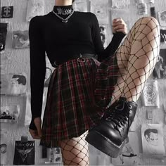 a woman in a black shirt and plaid skirt with fishnet stockings is posing for the camera