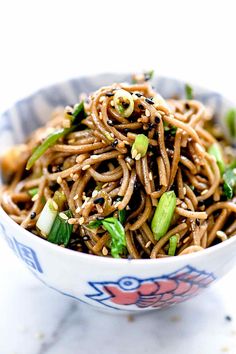 a bowl filled with noodles and vegetables on top of a marble countertop in front of a white background