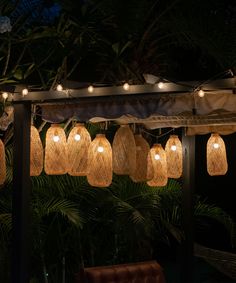 some lights are hanging from the roof of a gazebo in front of trees and plants