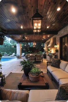 an outdoor living area with couches, tables and lamps on the ceiling is lit by lanterns