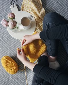 a woman is knitting on the floor next to a cup of coffee and some yarn