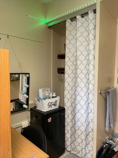 a bathroom with a white shower curtain next to a black trash can and wooden desk