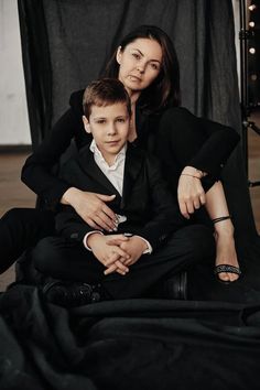 a woman sitting next to a boy in a black suit and white shirt on a chair