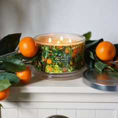 an orange scented candle sitting on top of a table next to some leaves and fruit