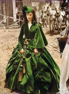 a woman in a green dress standing next to a man with a horse behind her